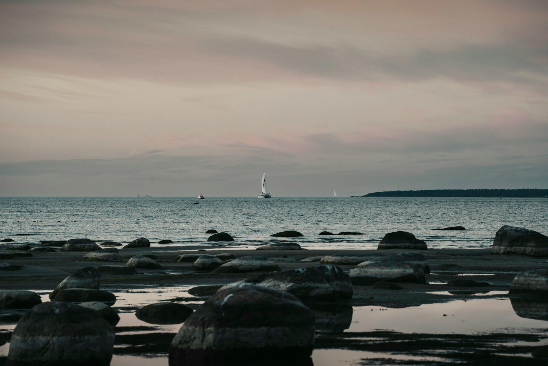 Zachód słońca nad Bałtykiem z żaglówkami i kamienistym brzegiem