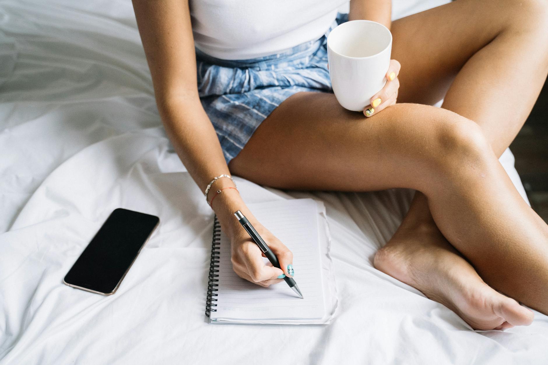 Kobieta w łóżku pije kawę i planuje weekend w notesie
