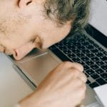 Wypalony pracownik opiera zmęczoną głowę na klawiaturze laptopa