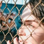 Zamyślona kobieta patrzy przez siatkę ogrodzenia w naturalnym świetle