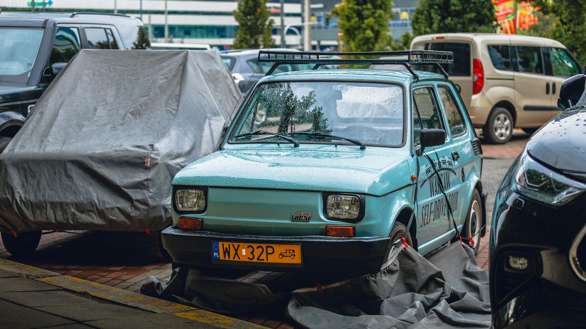 Maluch Fiat 126p na deszczu wśród nowoczesnych aut w Kutnie