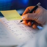 Dłoń zapisująca listę priorytetów w notesie z checkboxami