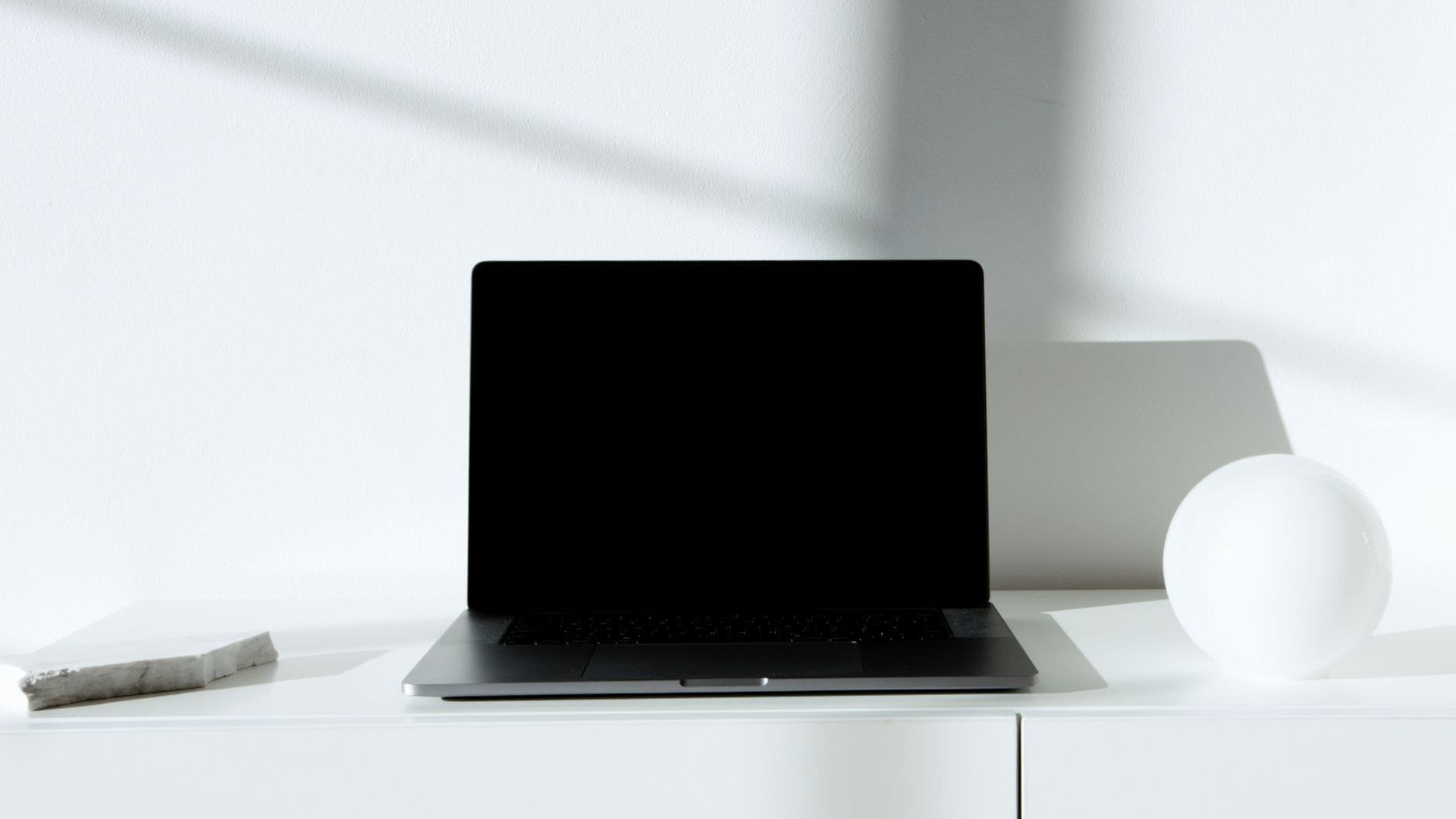 Czarny laptop na białym biurku w minimalistycznym, jasno oświetlonym wnętrzu